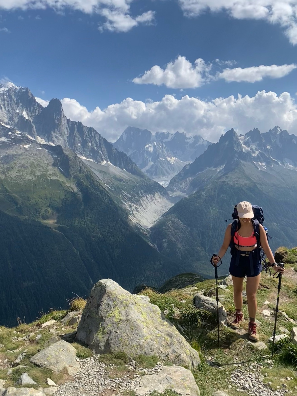 A hiker on an alpine ridge trail looking out over snow-capped peaks and a glacier valley.